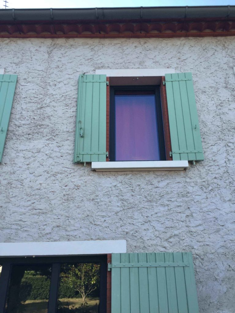 Fenêtre et volets verts sur une façade en pierre
