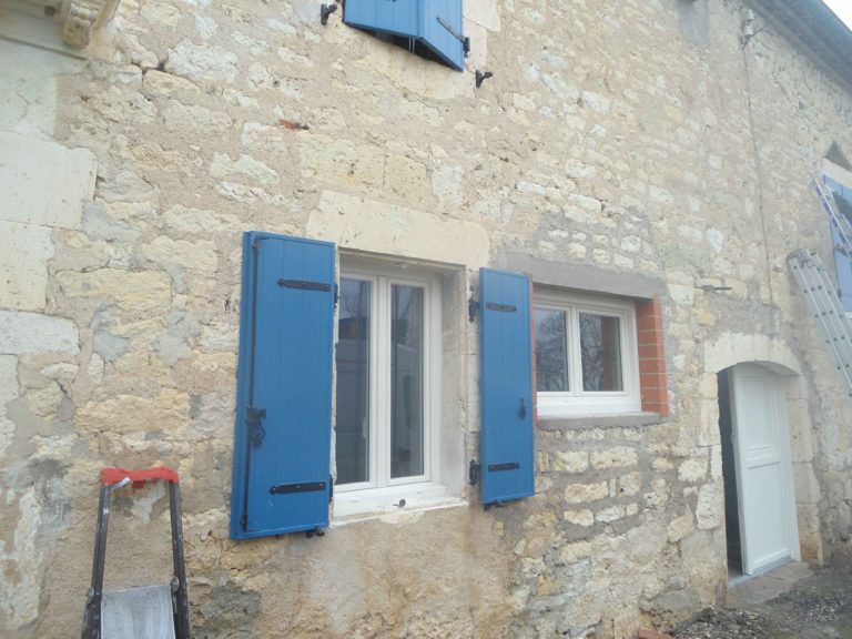 Fenêtres blanches et volets bleus sur une maison en pierre