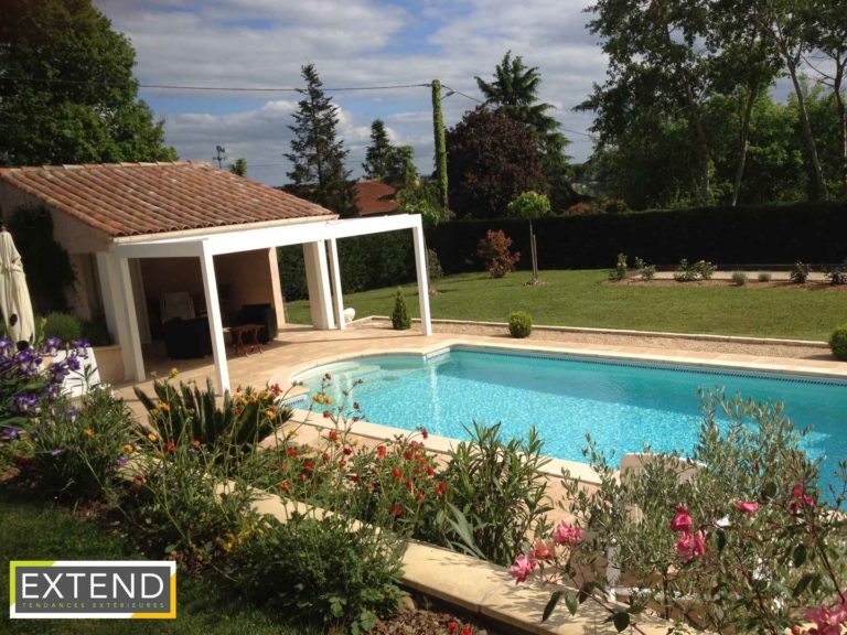 Pergola blanche au bord d'une piscine dans un jardin fleuri