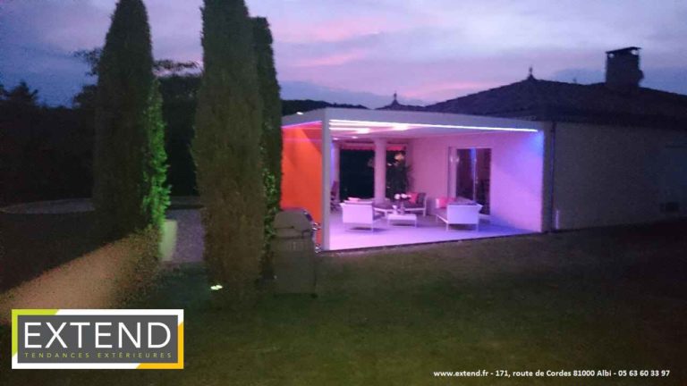 Pergola éclairée en LED violettes dans un jardin, à la tombée de la nuit