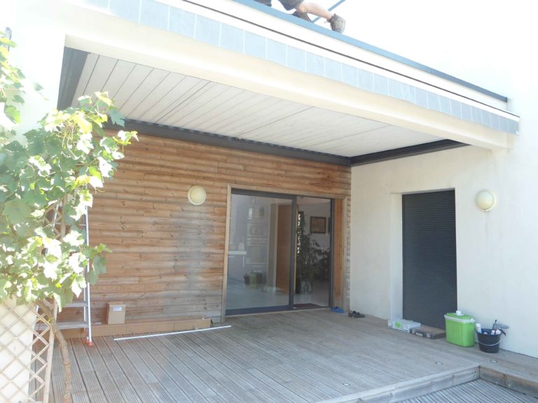 Pergola blanche devant une façade en bardage bois
