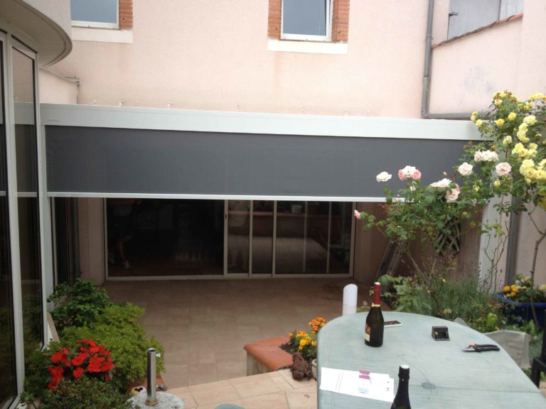 Screen anthracite baissé sous une pergola, terrasse fleurie