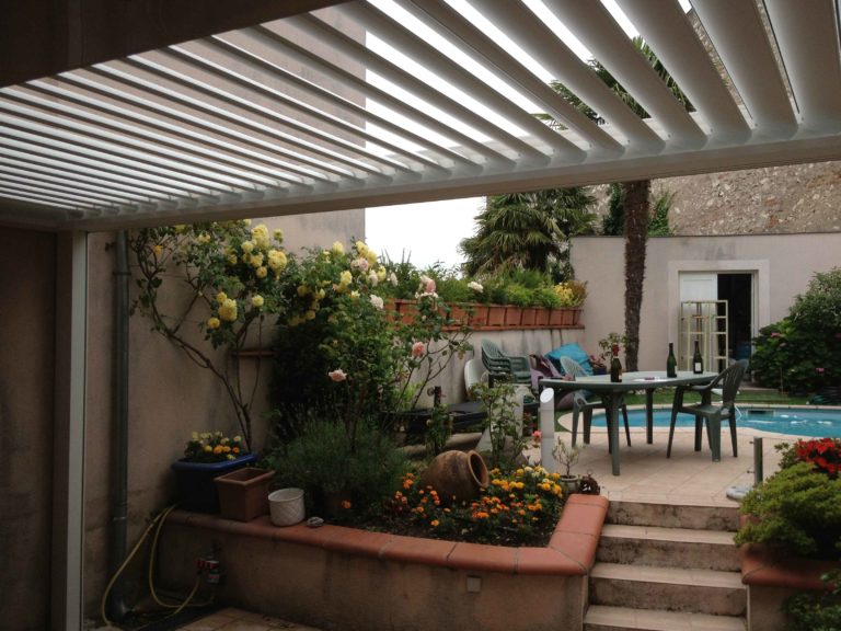 Lames orientables blanches au-dessus d'une terrasse fleurie près d'une piscine