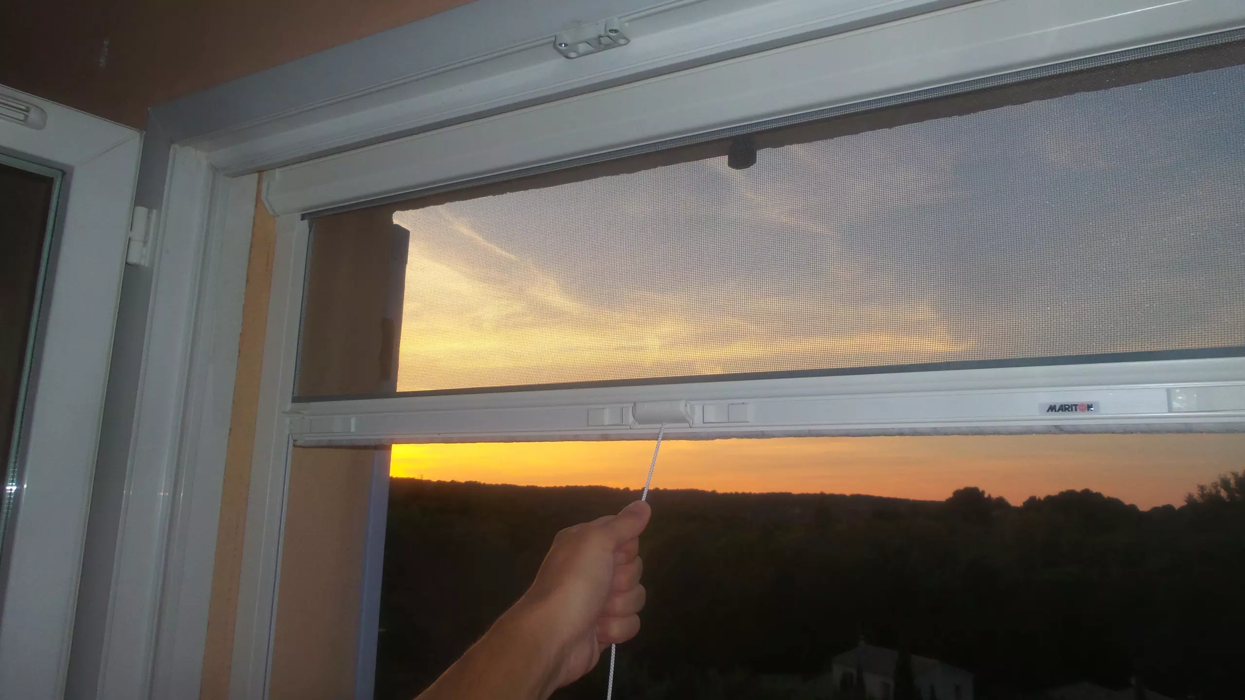 Moustiquaire enroulable déroulée devant une fenêtre au coucher du soleil