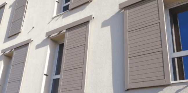 Volets coulissants entrouverts sur la façade d’un immeuble moderne.