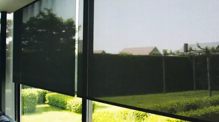 Store intérieur tamisant baissé sur de grandes baies vitrées avec vue sur un jardin lumineux.