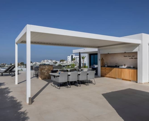 Terrasse moderne avec pergola adossée, cuisine extérieure et salle à manger en plein air.