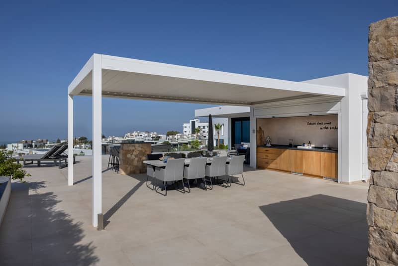 Terrasse moderne avec pergola adossée, cuisine extérieure et salle à manger en plein air.
