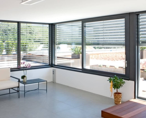 Intérieur moderne et lumineux avec de grandes baies vitrées et stores extérieurs, offrant une vue sur un jardin aménagé.