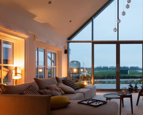 Salon moderne lumineux avec de grandes baies vitrées offrant une vue panoramique sur la campagne.