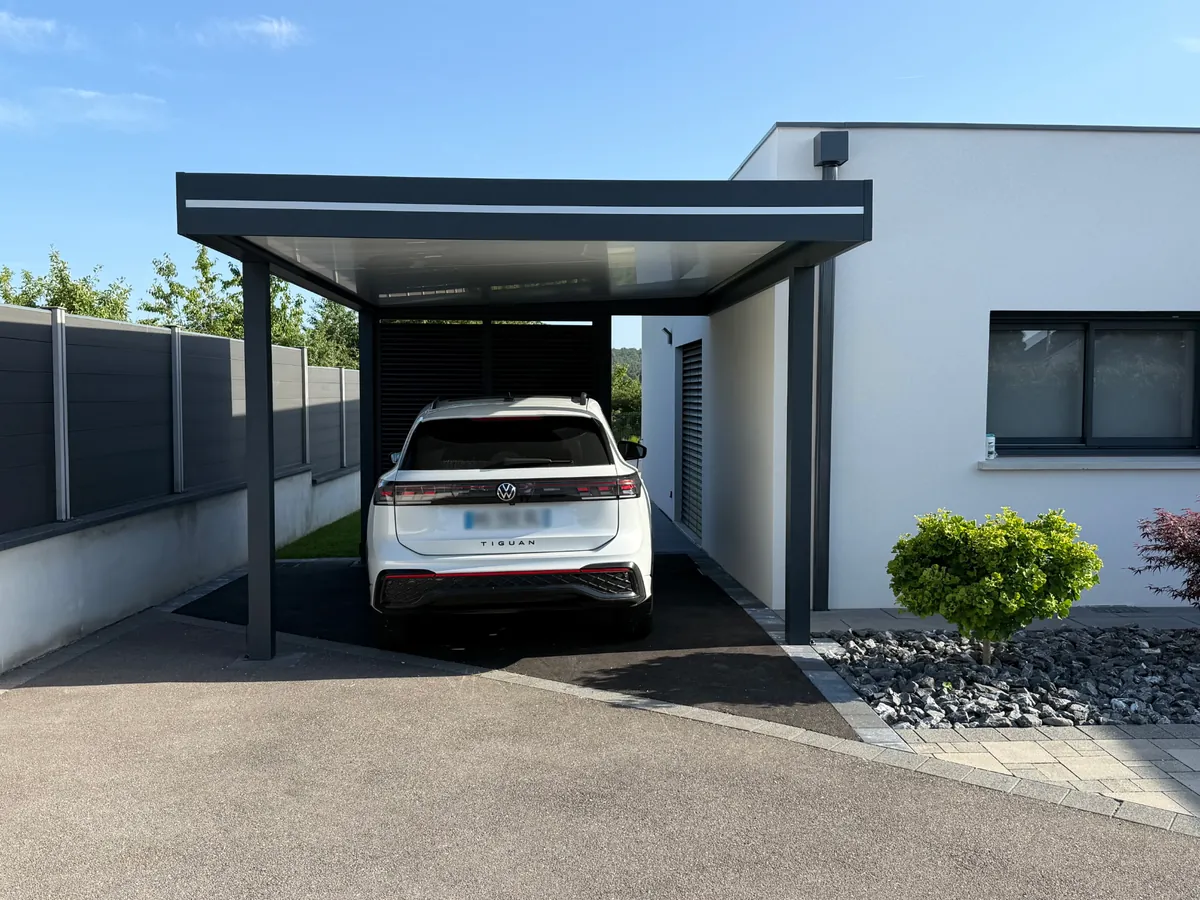 Carport aluminium adossé à une maison blanche, fond fermé par des lames