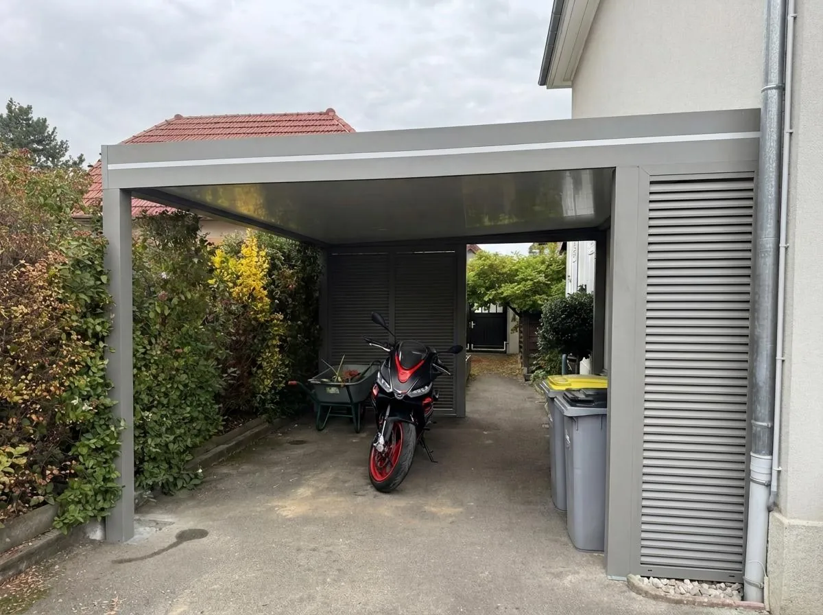 Carport aluminium gris fermé sur un côté par des lames, une moto rangée dessous
