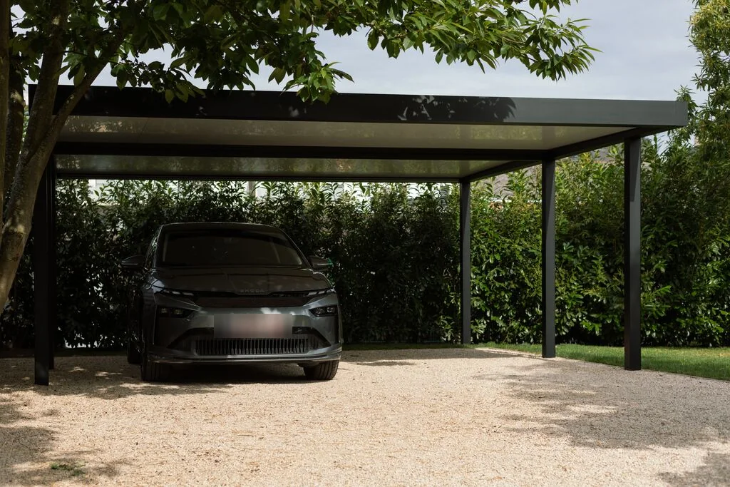 Carport en aluminium Brustor B910 à toit plat, une voiture à l’abri devant une haie