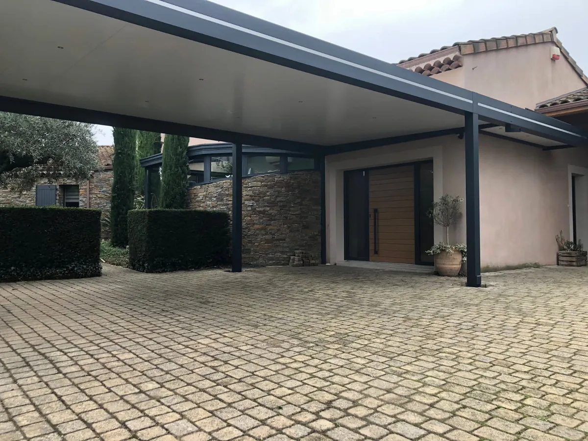 Carport aluminium de grande largeur adossé à une maison, cour pavée