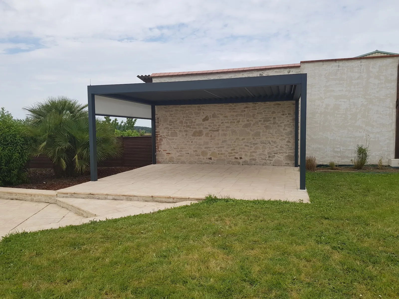 Pergola bioclimatique anthracite adossée à un mur en pierre