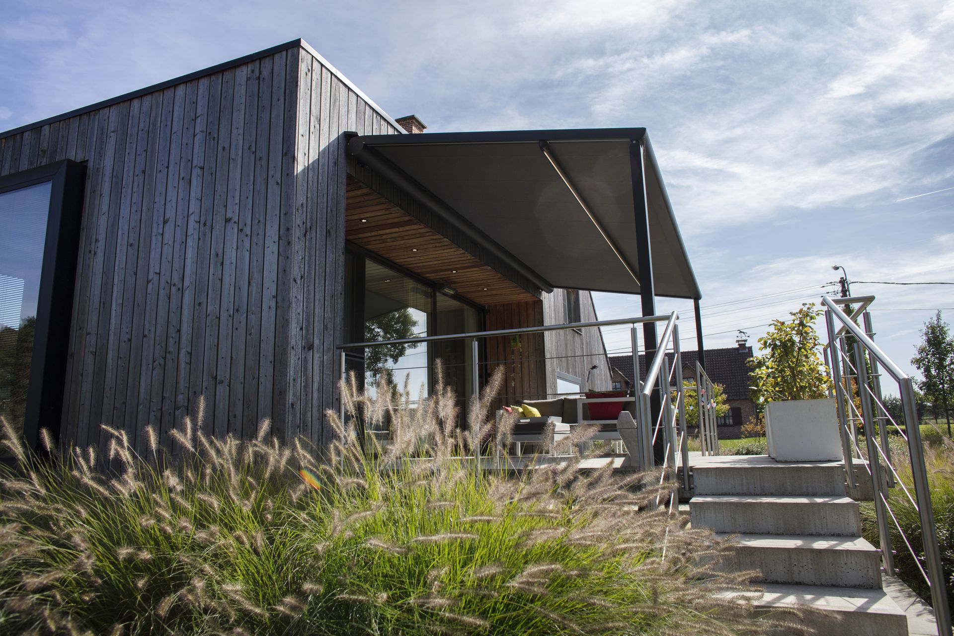 Pergola Brustor B128 devant une maison en bois noir côté jardin