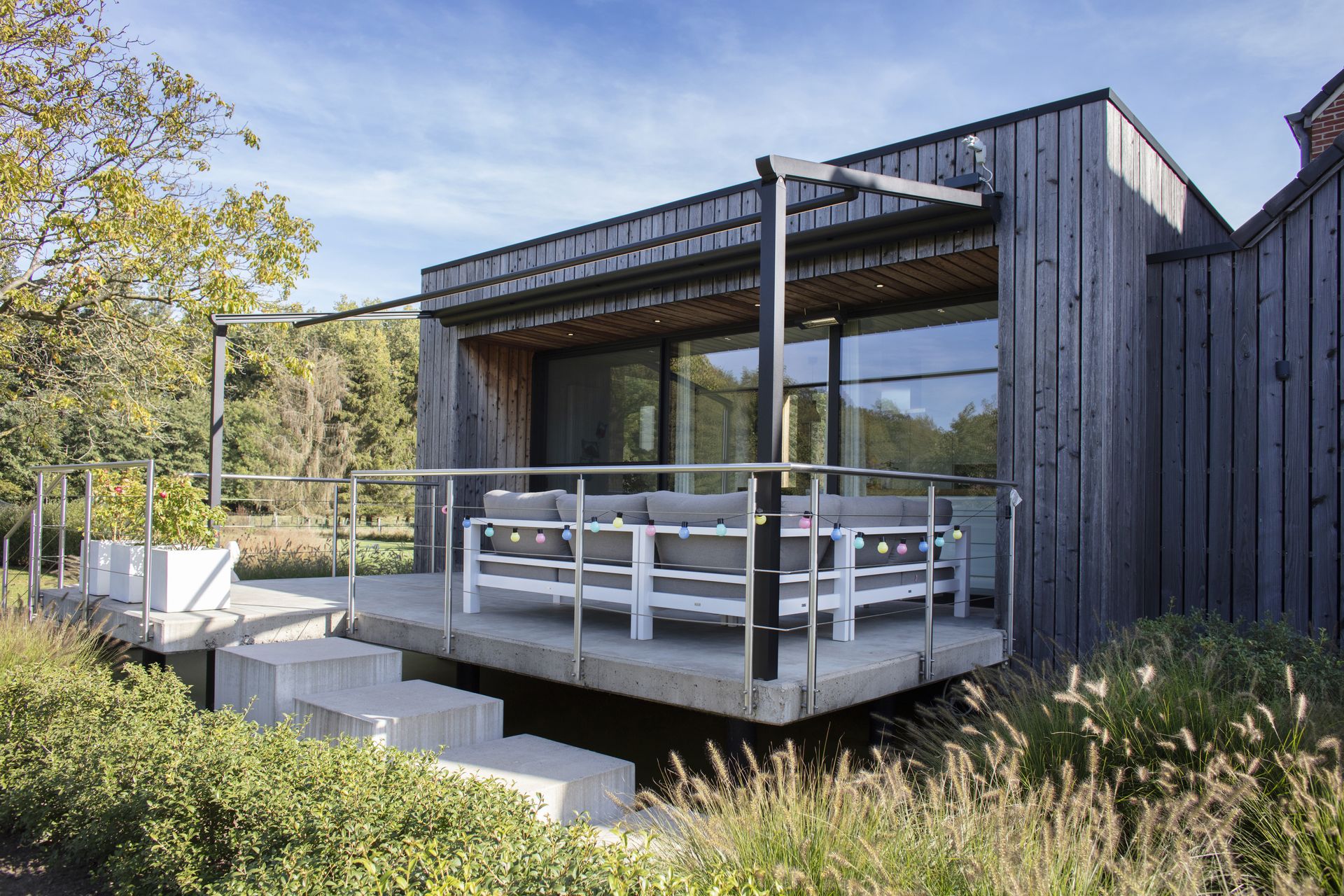 Pergola Brustor B128 devant une maison en bois noir avec terrasse