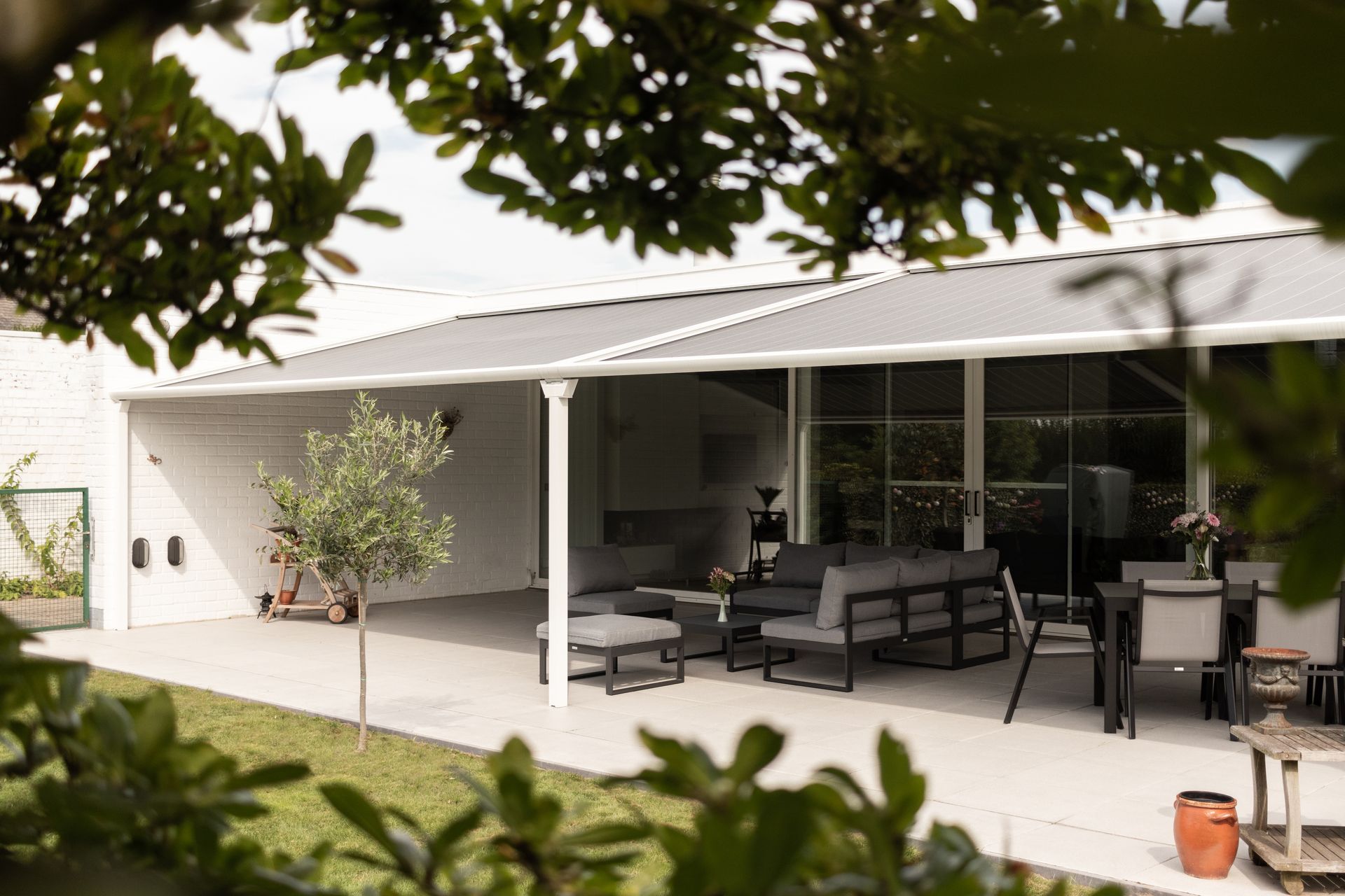 Pergola Brustor B128 sur une terrasse blanche avec salon d'extérieur