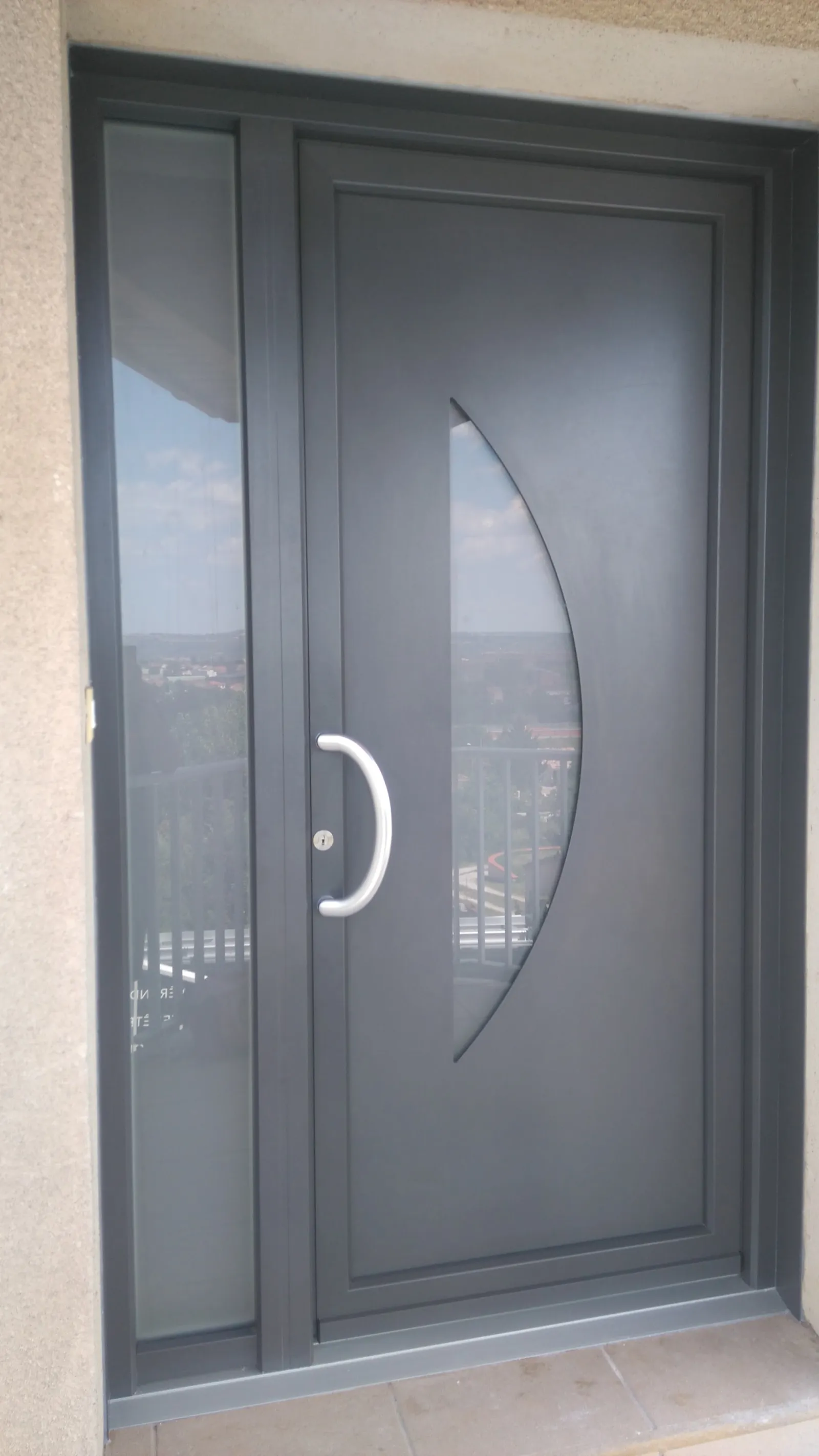 Porte d’entrée grise avec vitrage en arc de cercle et poignée tubulaire
