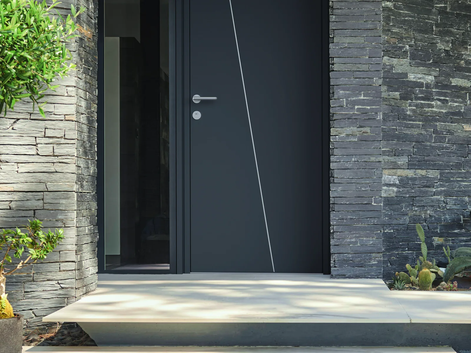 Porte d’entrée aluminium K-Line pleine anthracite entre deux murs en pierre