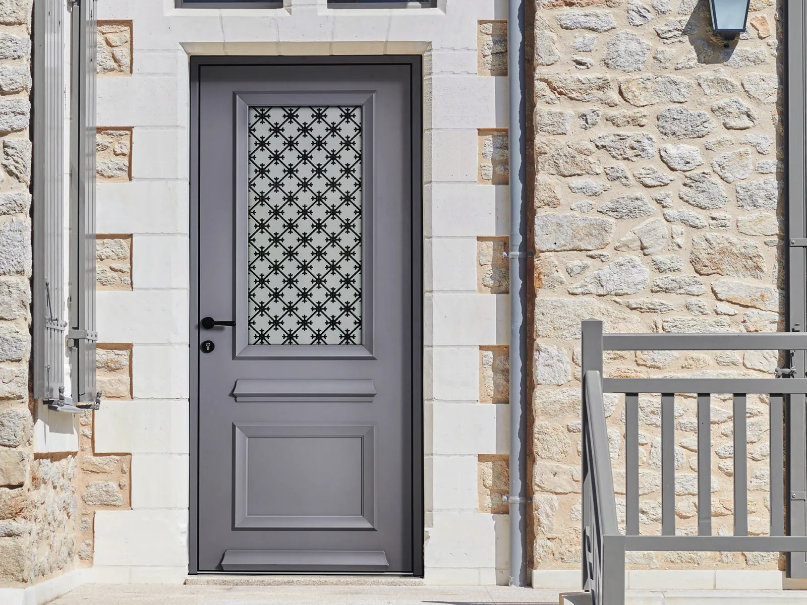 Porte d’entrée traditionnelle K-Line grise à grille sur une maison en pierre