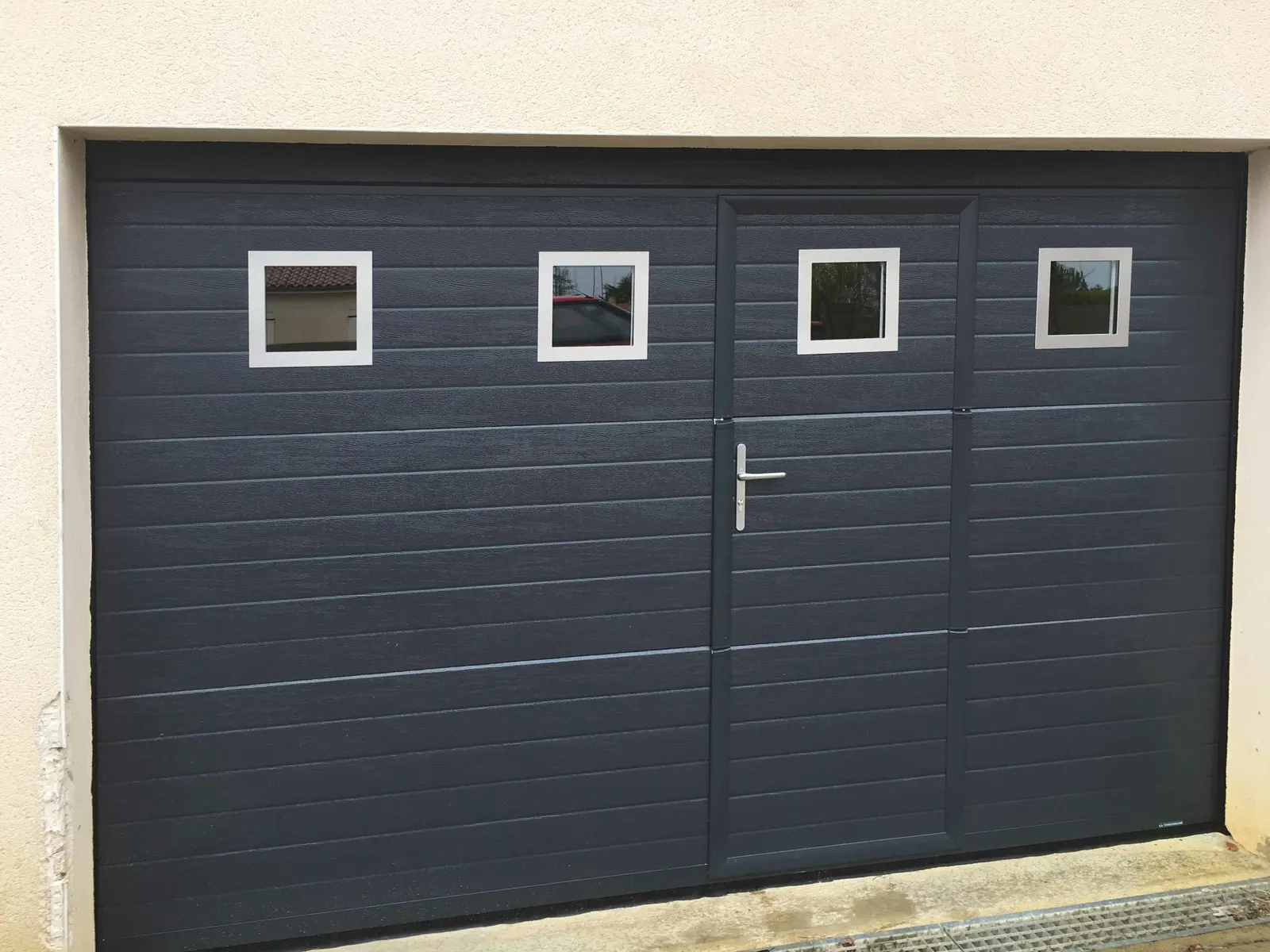 Porte de garage sectionnelle anthracite avec hublots carrés et portillon