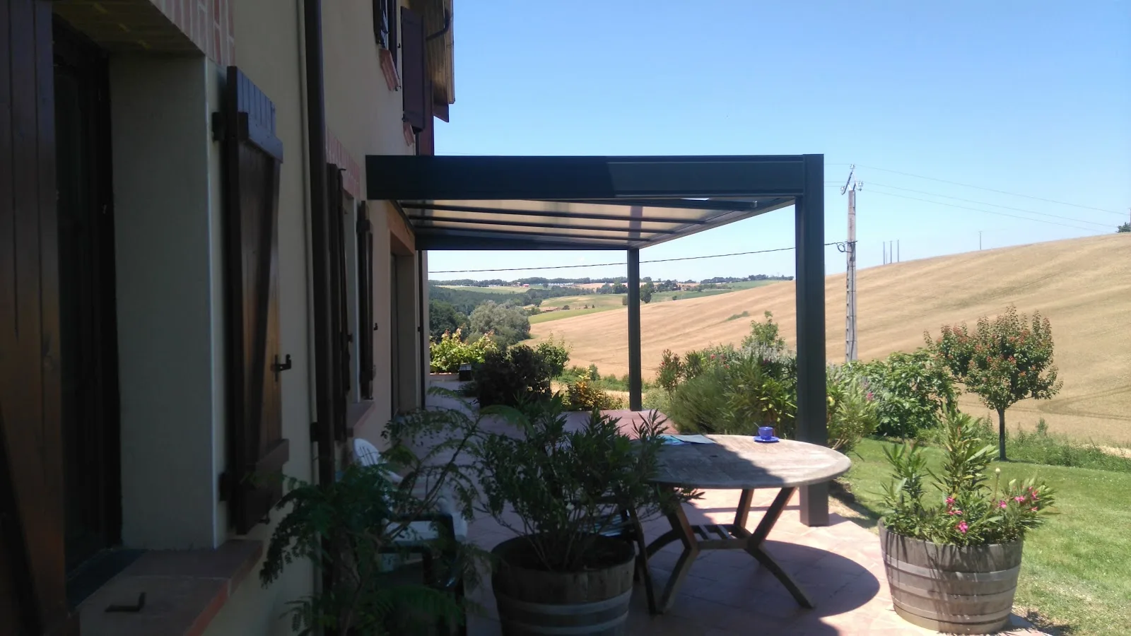 Préau anthracite prolongeant la terrasse face à la campagne