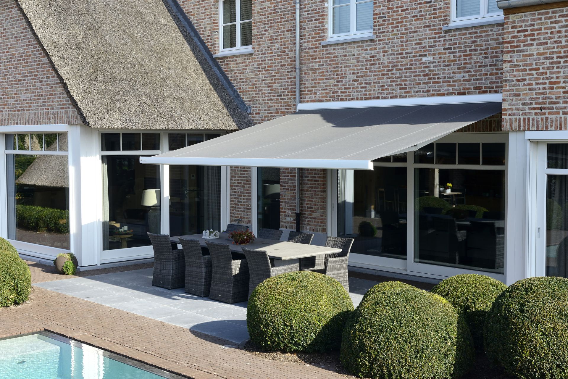 Store banne Brustor B24 à toile grise sur une maison en brique avec piscine