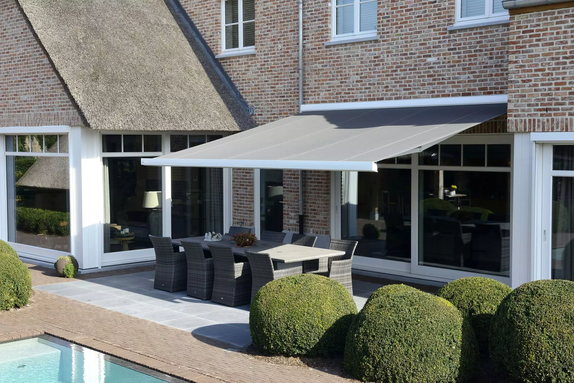 Store banne Brustor B24 sur une maison en brique au bord d'une piscine