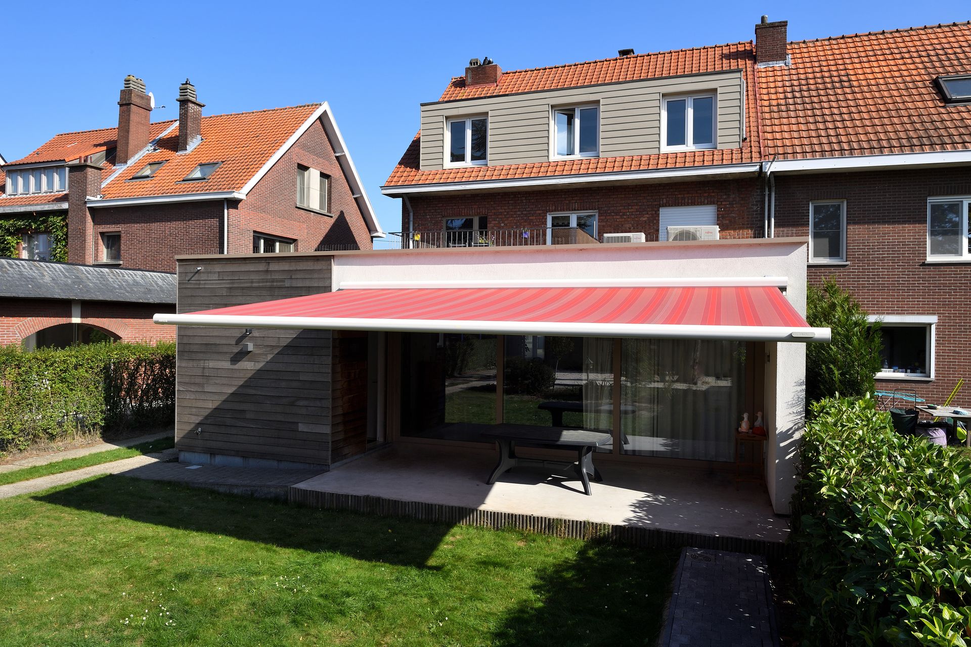 Store banne Brustor B25 à toile rouge rayée sur une annexe en bois
