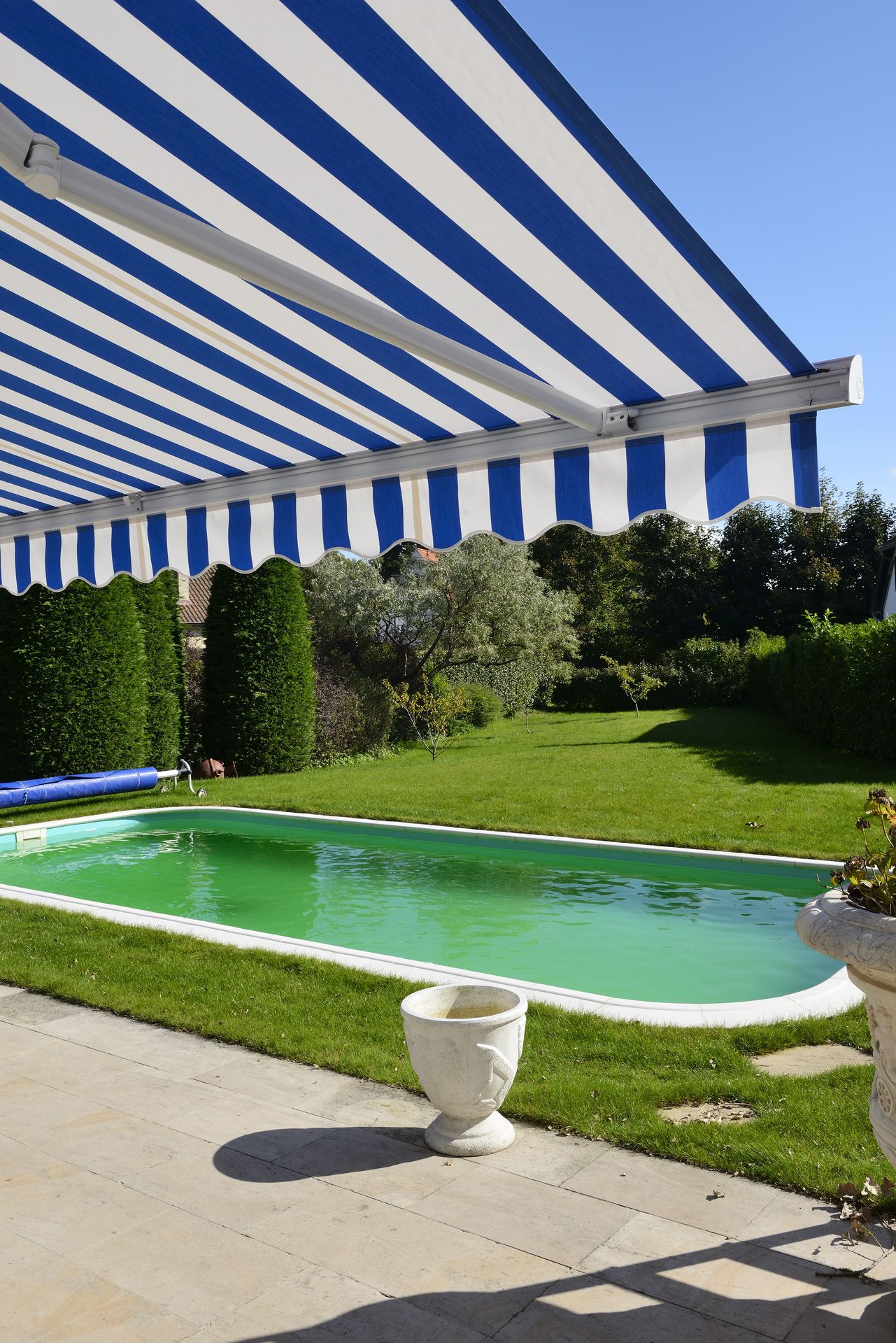 Store banne Brustor B35 à toile rayée bleue et blanche au-dessus d'une piscine