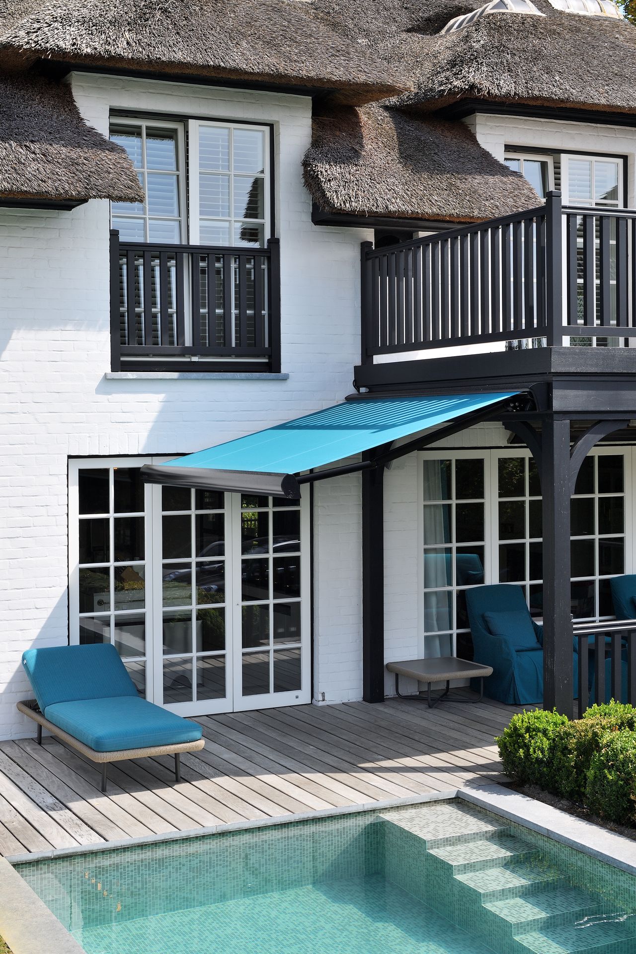 Store banne Brustor B38 à toile turquoise au-dessus d'une terrasse en bois avec bassin