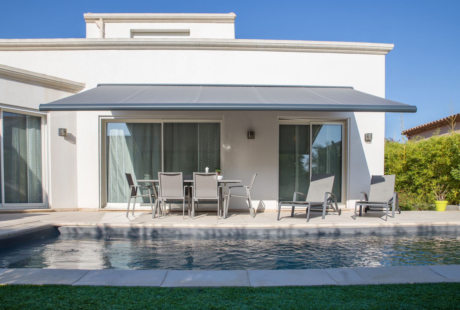 Store banne Brustor B50 XL à coffre fermé sur une façade blanche au bord d'une piscine