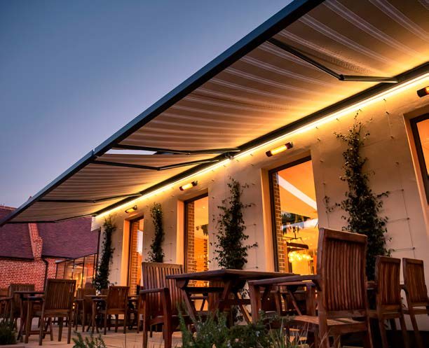 Store banne Brustor éclairé par des LED et chauffé par des radiants sur une terrasse de restaurant le soir