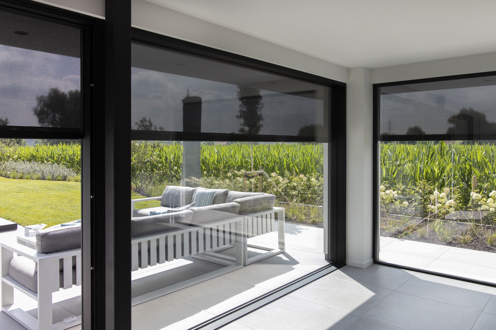 Vue sur le jardin depuis le séjour à travers des screens ZIP Brustor B1200 baissés
