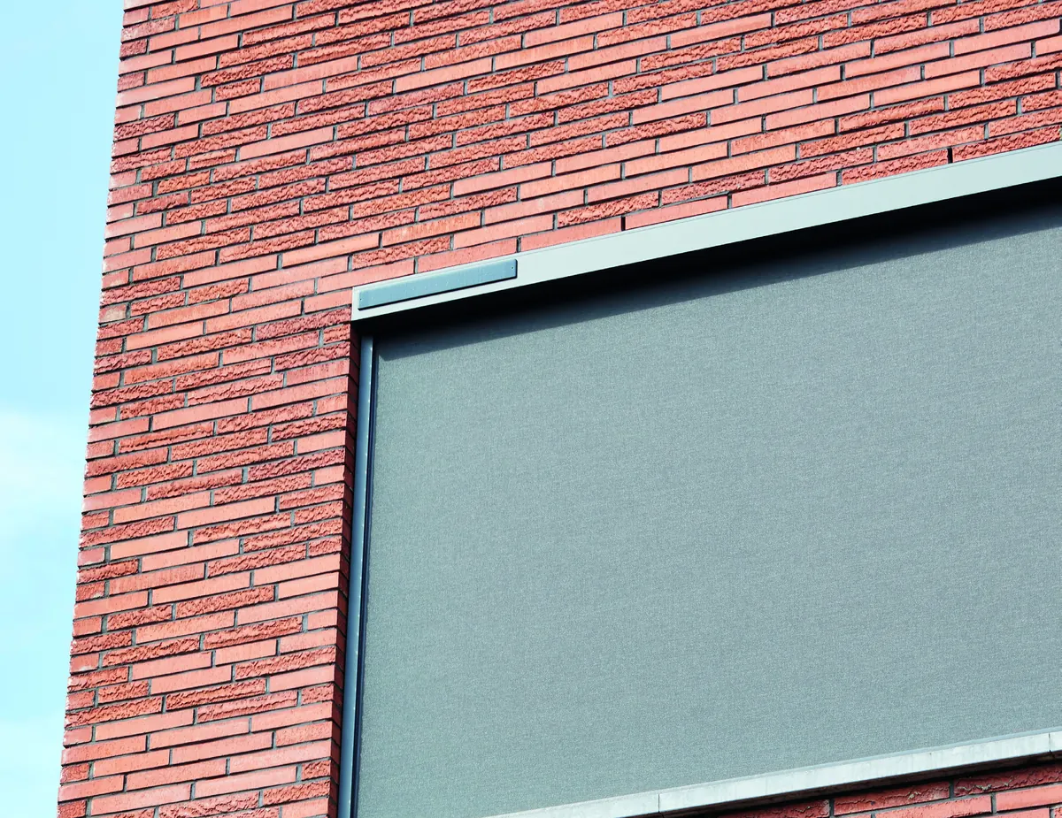 Store vertical ZIP solaire descendu devant une fenêtre, façade en brique