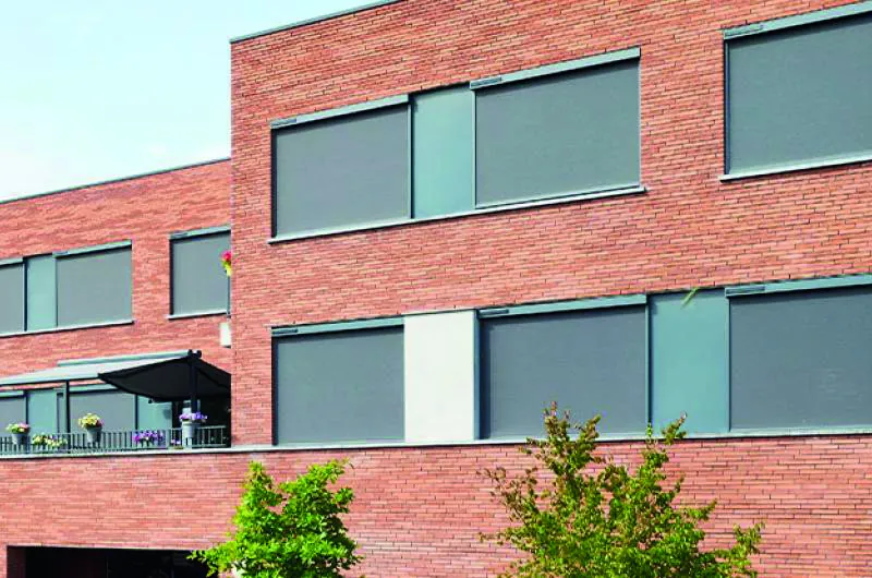 Façade d'immeuble en brique équipée de screens ZIP solaires et d'un store banne de balcon