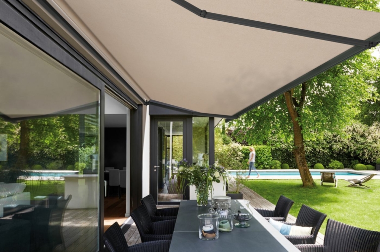 Store banne avec toile Dickson beige au-dessus d'une terrasse avec piscine