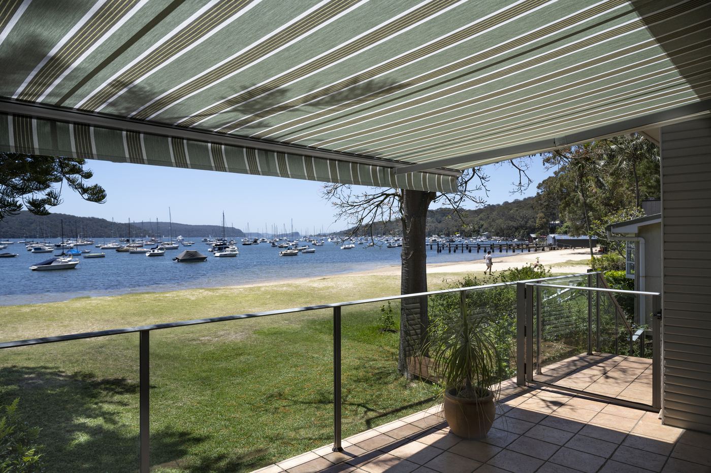 Store banne à toile Dickson rayée verte sur une terrasse en bord de mer