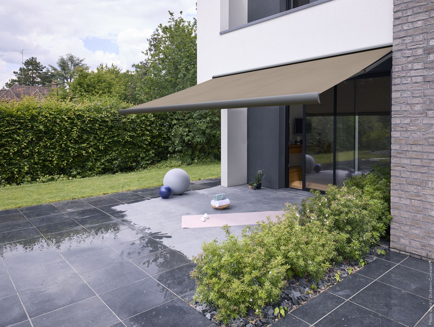 Store banne à toile Dickson taupe sur une maison donnant sur le jardin